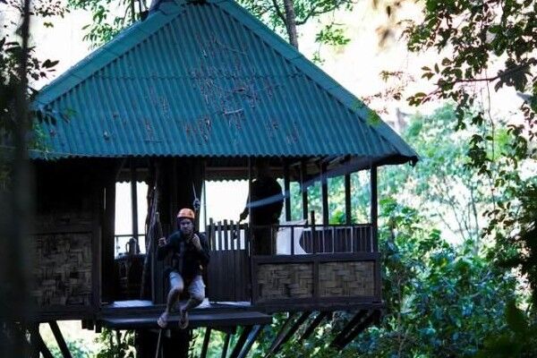A man dangling from a zipwire that's attached to a treehouse
